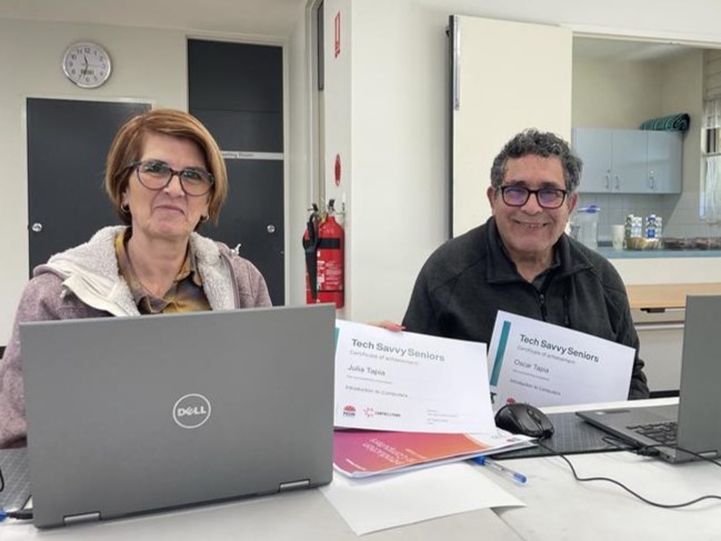 Two people smiling in front of laptops